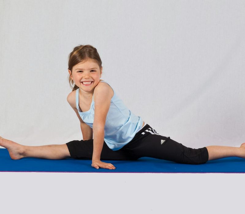 A young girl laughing while attempting a playful yoga pose on a colorful mat.
